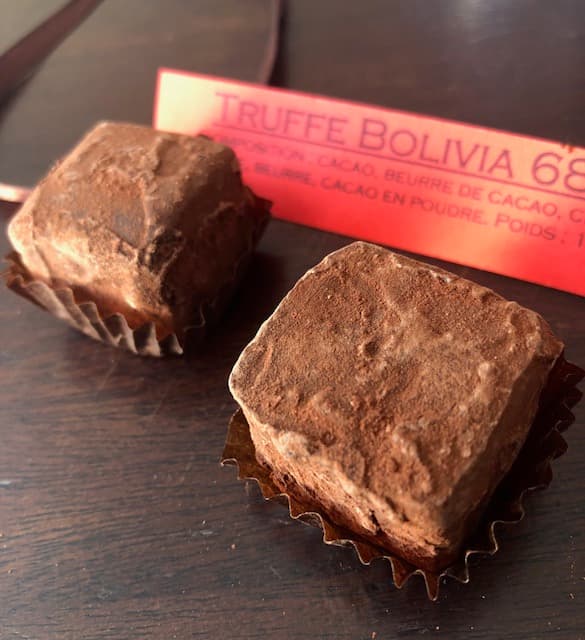 Deux Truffes Bolivia enrobées de cacao en poudre, avec leur étiquette rose indiquant le nom et la composition du chocolat