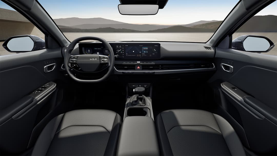 Habitacle de la Kia K4 Sportswagon avec écrans numériques panoramiques, volant et sièges noirs, vue dégagée sur un lac et des montagnes