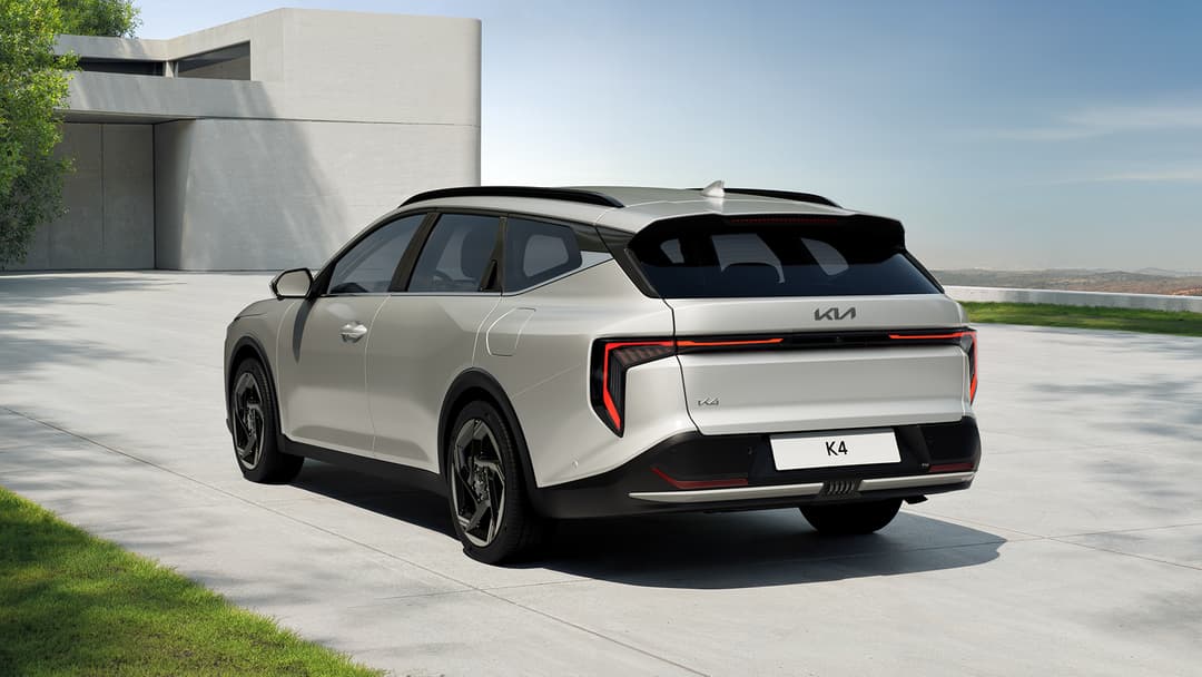 Kia K4 Sportswagon blanc nacré de profil sur une terrasse, avec un bâtiment moderne en arrière-plan