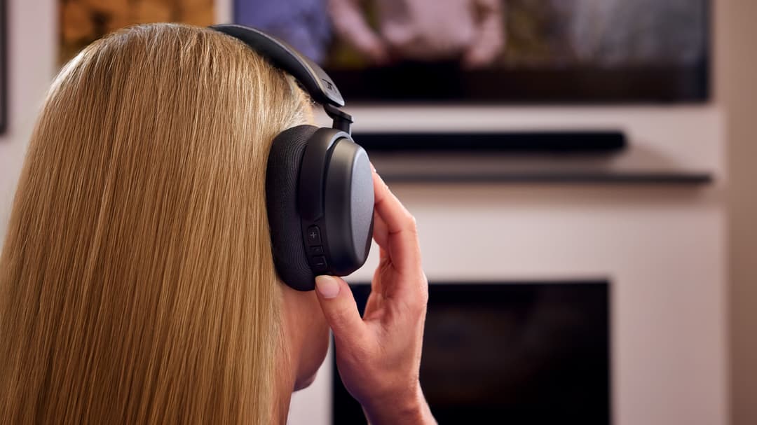 Personne portant un casque audio noir devant un téléviseur, de profil avec cheveux blonds longs