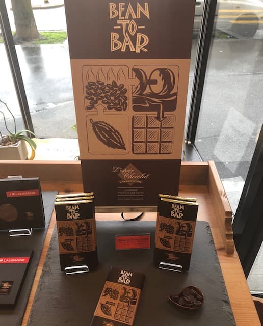 Vitrine de l'Espace Chocolat présentant le projet Bean To Bar avec affiche marron, paquets de chocolat et fèves de cacao importées du Cameroun