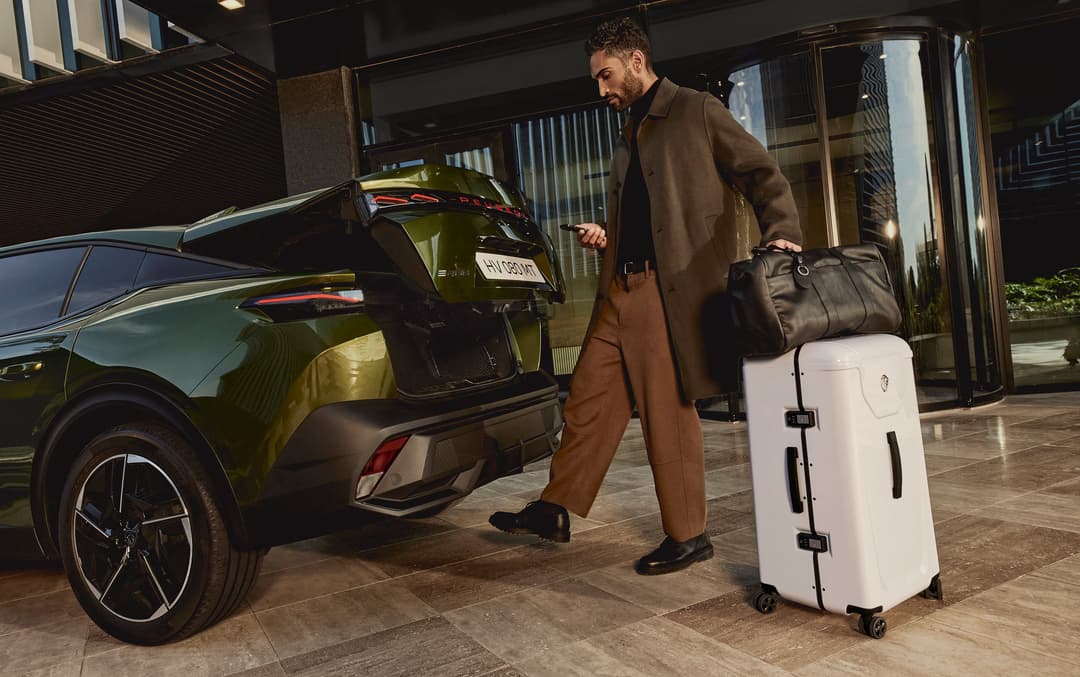 Homme chargeant ses bagages dans le coffre d'une Peugeot 408 vert anis, devant un immeuble moderne