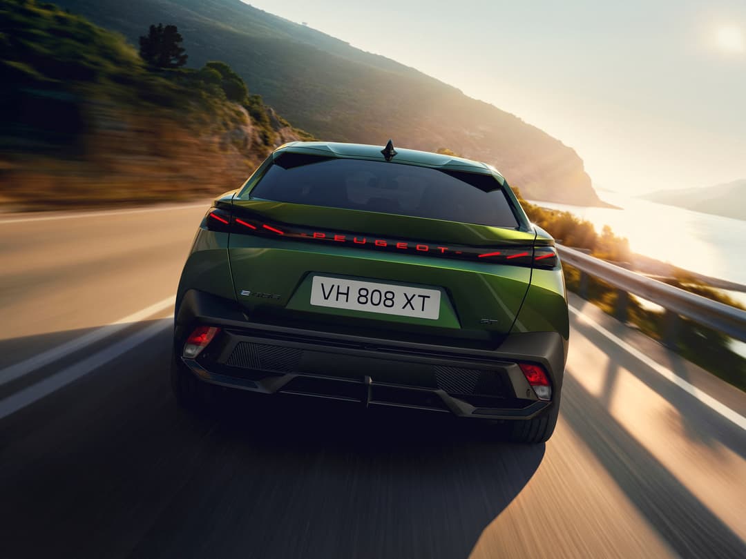 Peugeot E-408 vert en mouvement sur une route côtière, vue de l'arrière avec feux rouges allumés et paysage montagneux