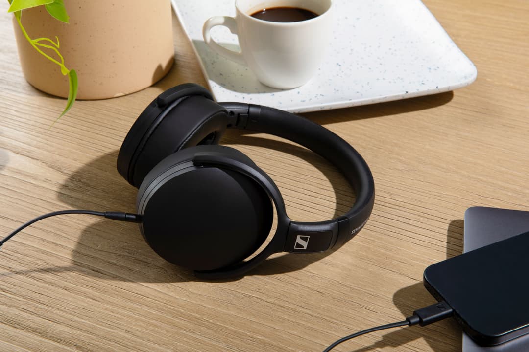 Casque Sennheiser HD 400U noir posé sur un bureau en bois clair, à côté d'une tasse de café et d'une plante