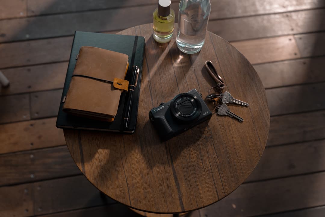 Canon PowerShot G7 X III posé sur une table ronde en bois avec carnet, stylo, clés et verre d'eau