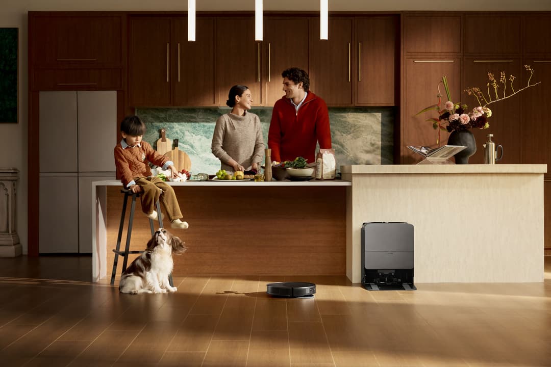 Robot aspirateur Saros 20 au design compact noir, en action dans une cuisine familiale avec trois personnes et un petit chien