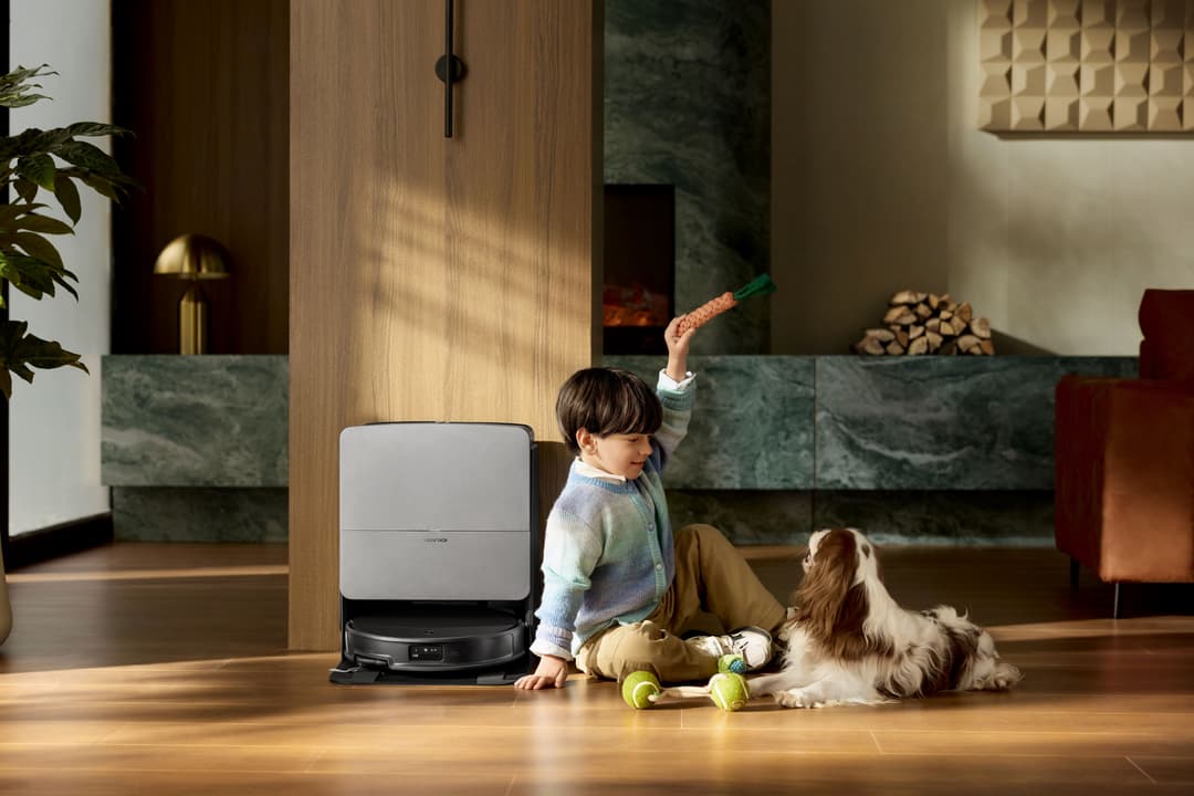 Robot aspirateur blanc et noir Saros 20 nettoyant un parquet près d'un enfant et d'un petit chien dans un salon moderne