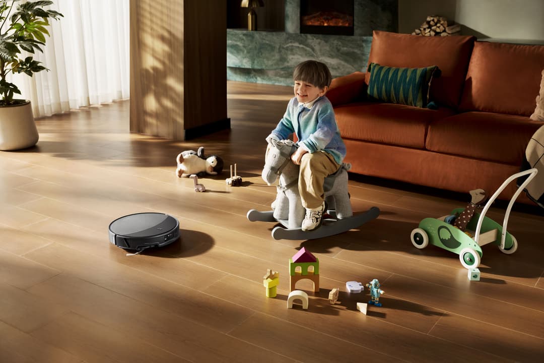 Robot aspirateur noir sur parquet, enfant jouant avec des jouets dans un salon lumineux avec canapé terracotta