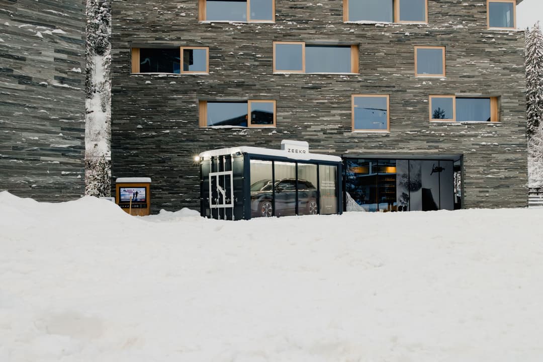 Showroom Zeekr implanté devant un bâtiment en pierre dans la neige à Laax, avec une voiture électrique visible à l'intérieur