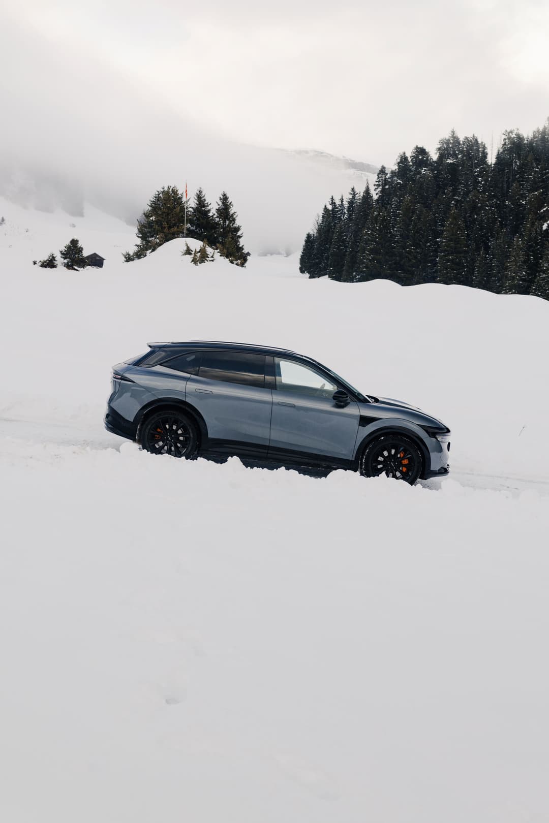 Zeekr bleu électrique dans un paysage enneigé montagneux avec sapins et brouillard