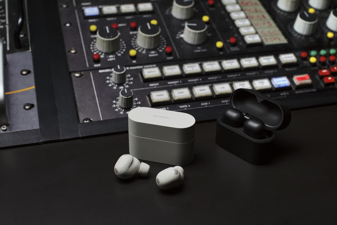 Écouteurs Sony WF-1000XM6 blancs sortis de leur boîtier, avec un modèle noir en arrière-plan sur une console audio professionnelle