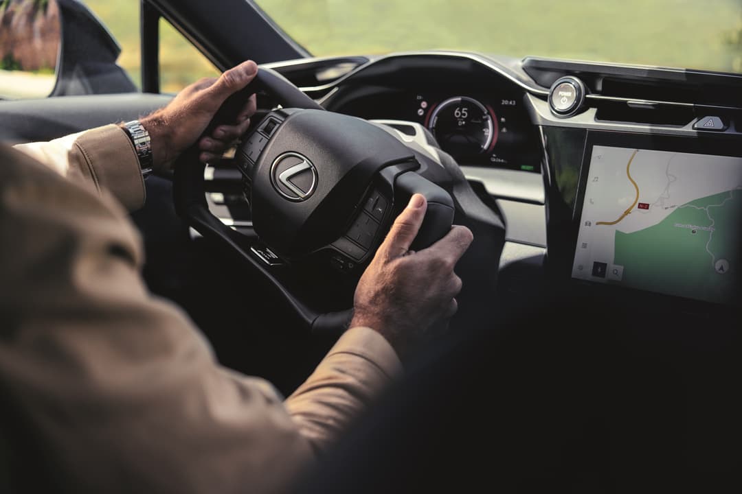 Conducteur tenant le volant Steer-by-wire de Lexus, habitacle avec écran de navigation et compteur digital