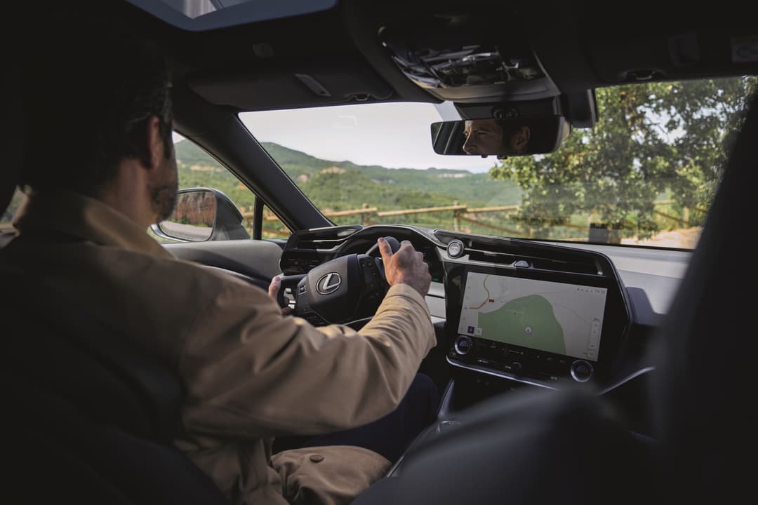 Conducteur tenant le volant compact d'une Lexus avec système Steer-by-wire, intérieur moderne avec écran tactile et large pare-brise dégagé
