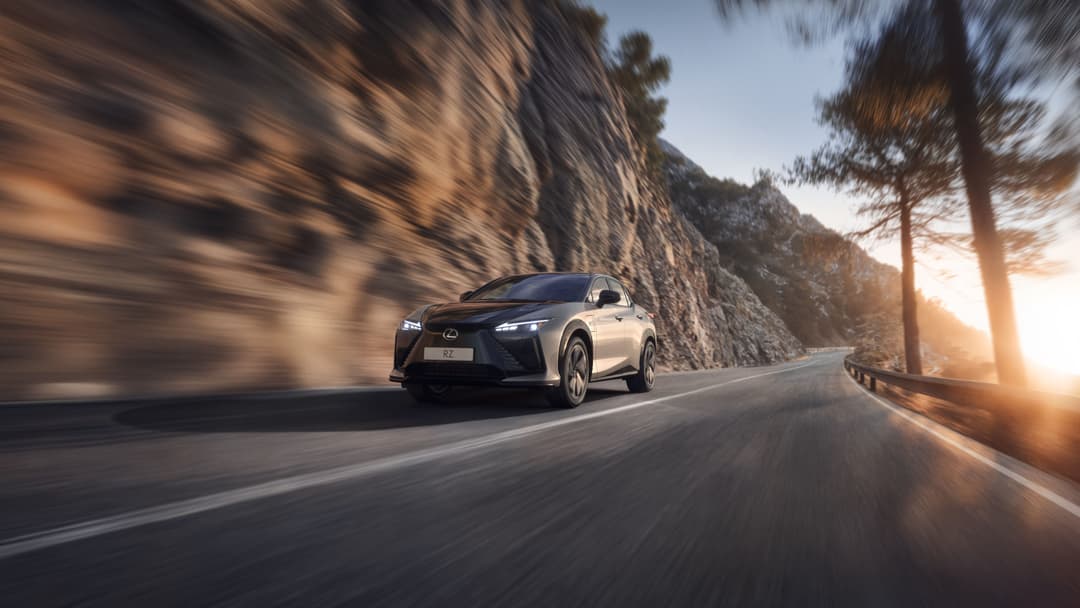 Lexus blanche roulant sur une route de montagne sinueuse au coucher de soleil, avec falaises rocheuses et pins en arrière-plan