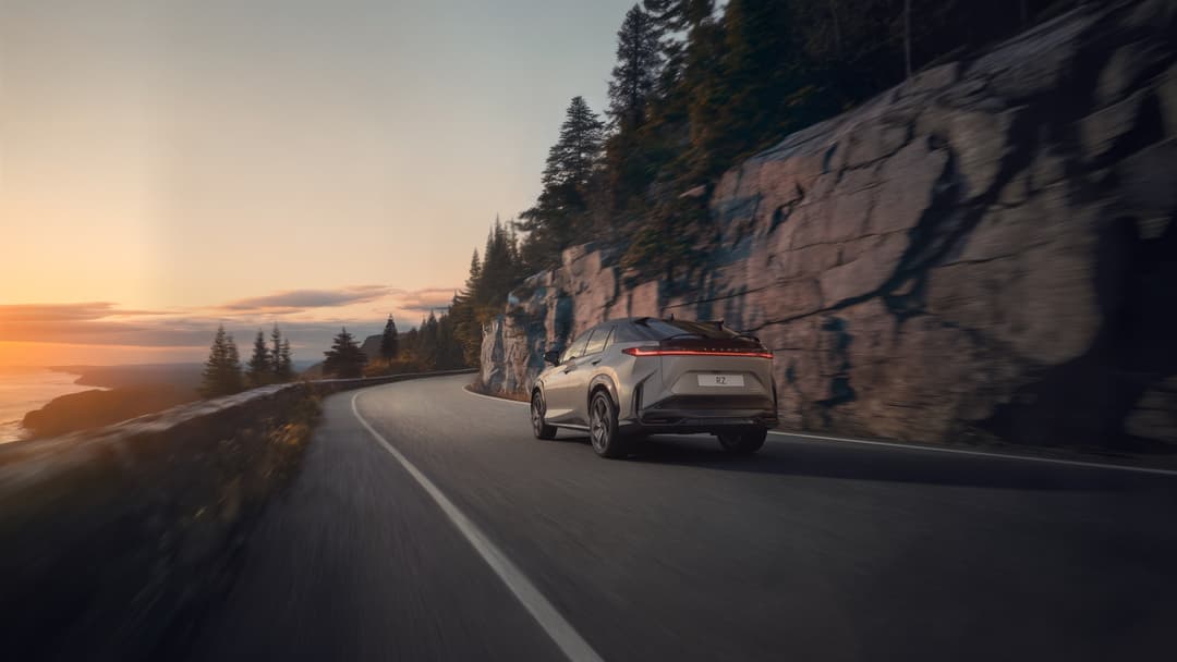 Lexus RZ 550e F SPORT blanc électrique roulant sur une route de montagne sinueuse au coucher du soleil