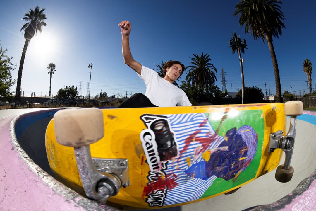 Skateur en l'air au-dessus d'une planche jaune colorée dans un skate-park, ciel bleu et palmiers en arrière-plan