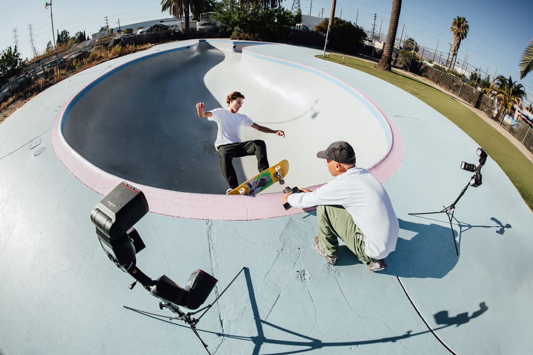 Skateur en action dans un skate park, photographié en ultra grand angle avec déformation fisheye, cadreur et équipement visible au premier plan