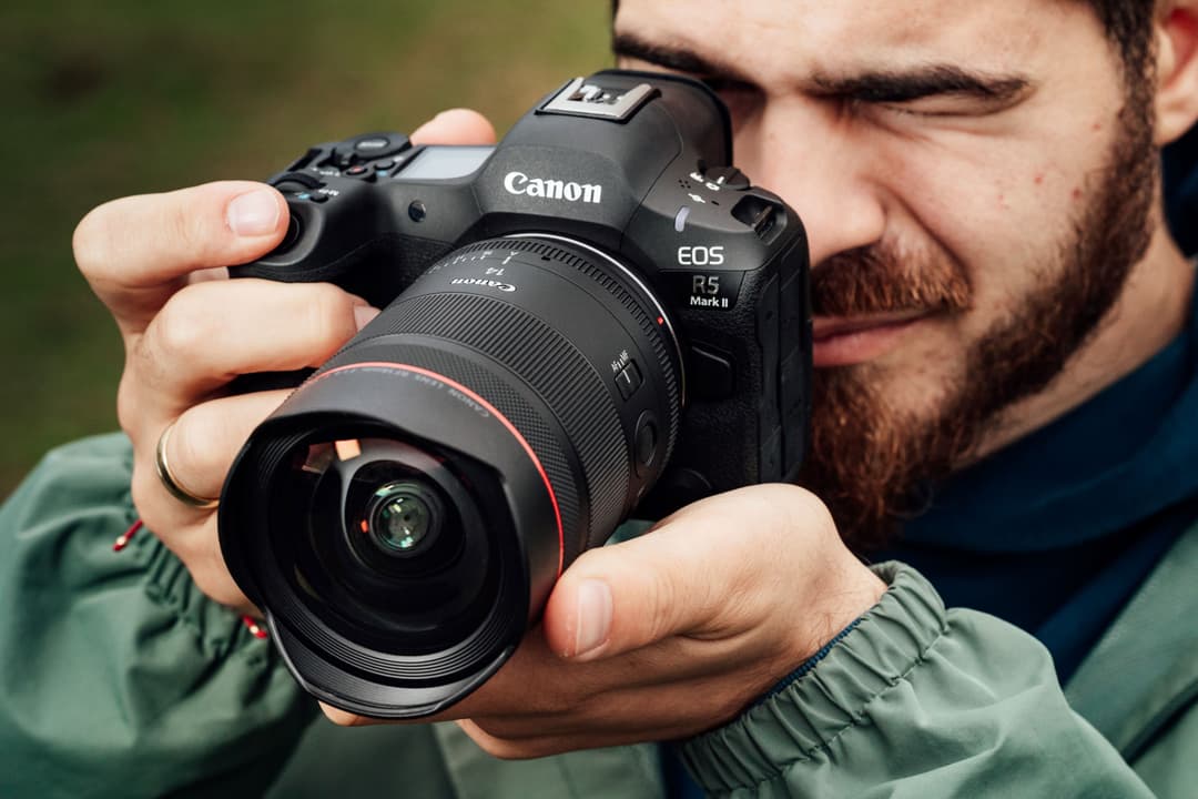 Canon EOS R5 Mark II avec objectif Série L tenu dans les mains d'un photographe portant une veste verte