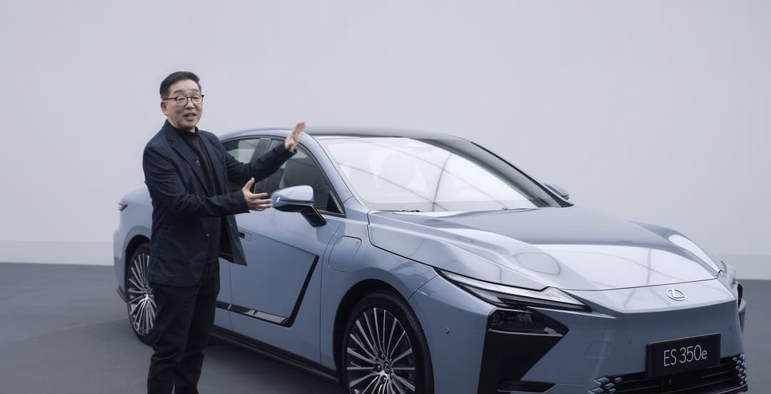Nouvelle Lexus ES grise présentée par un homme en costume noir, portière ouverte, sur fond blanc