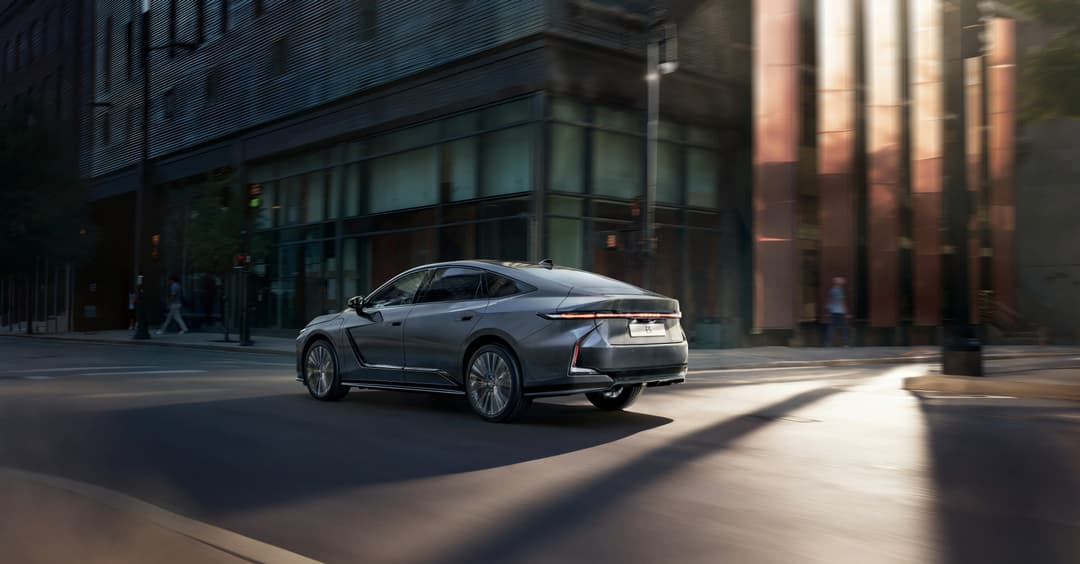 Nouvelle Lexus ES grise de profil dans une rue urbaine, montrant l'arrière avec sa barre lumineuse caractéristique en L et logo Lexus