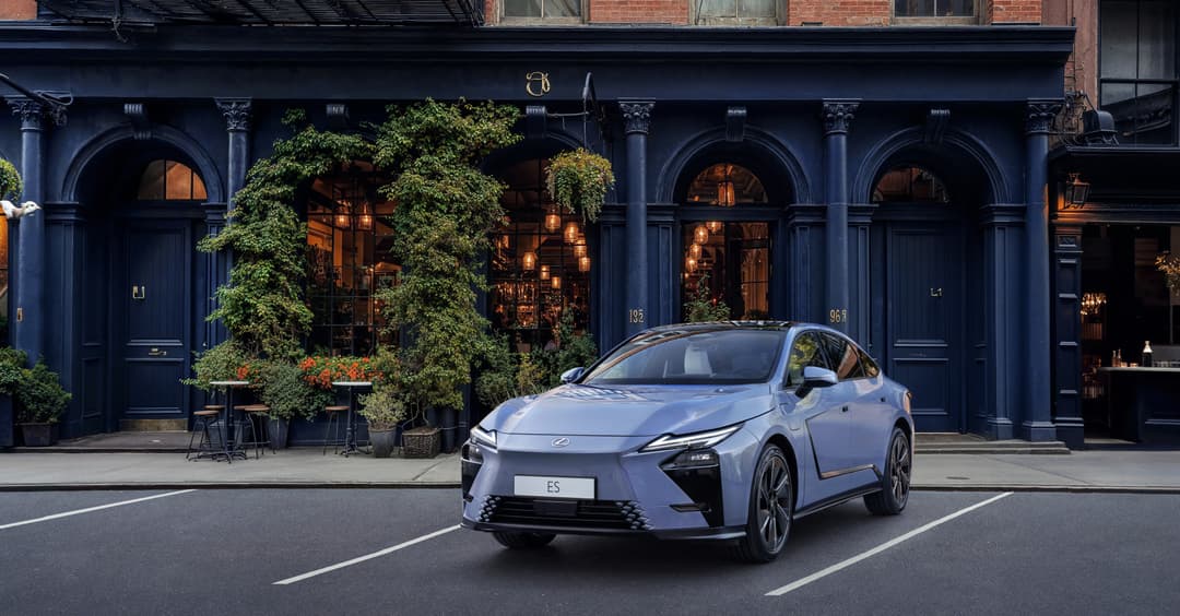 Lexus ES blanche garée devant une façade bleue avec colonnes et devanture de boutique illuminée, lierre grimpant et jardinières