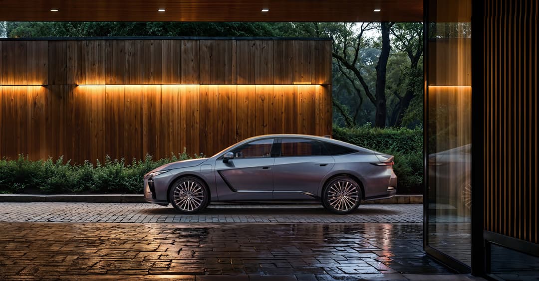 Lexus ES berline grise garée devant un mur en bois illuminé par des appliques dorées, dans un cadre architectural moderne avec sol mouillé