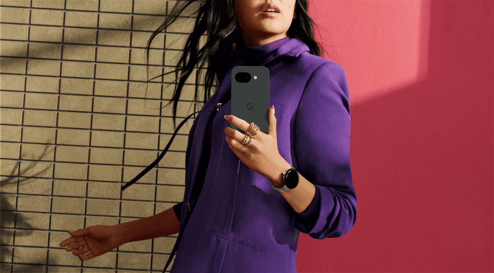 Google Pixel 10a de couleur gris sombre, tenu à la main par une femme vêtue d'un blazer violet