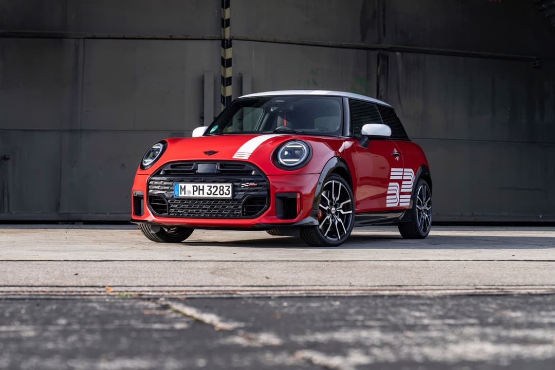 MINI 1965 Victory Edition rouge avec bande blanche, toit noir et détails gris, stationnée devant un mur de béton