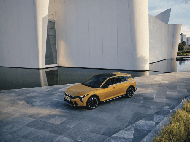 Kia K4 jaune garée devant une architecture moderne blanche avec plan d'eau