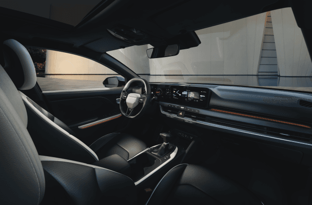 Intérieur de la Kia K4 avec tableau de bord moderne, volant et sièges en cuir gris clair, vue depuis le siège passager