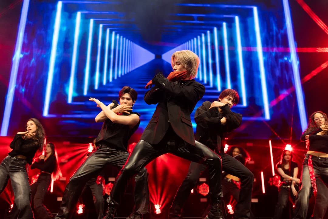 Groupe de danseurs en tenue noire performant sur scène avec décor de néons bleus et rouges