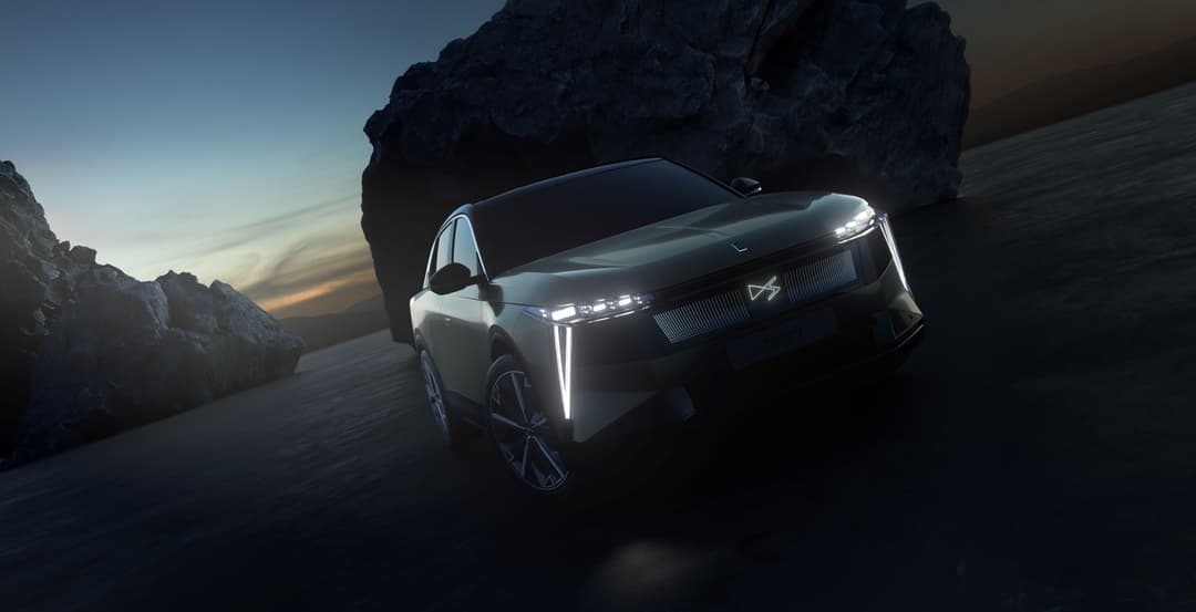 DS N°7 E-TENSE, SUV électrique blanc aux phares futuristes, en position trois-quarts face au coucher de soleil, décor rocheux en arrière-plan