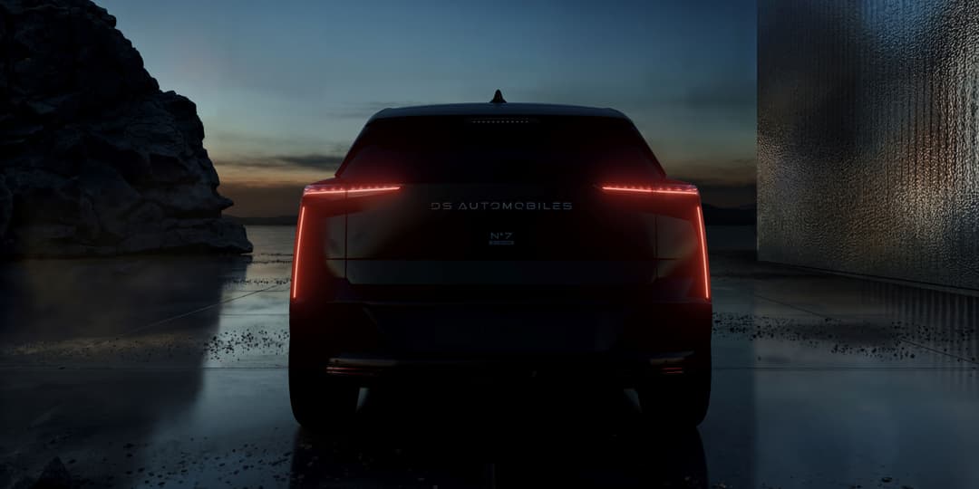 DS N°7 SUV vu de l'arrière, feux rouges allumés, stationné sur une plage entre falaise et structure architecturale au crépuscule