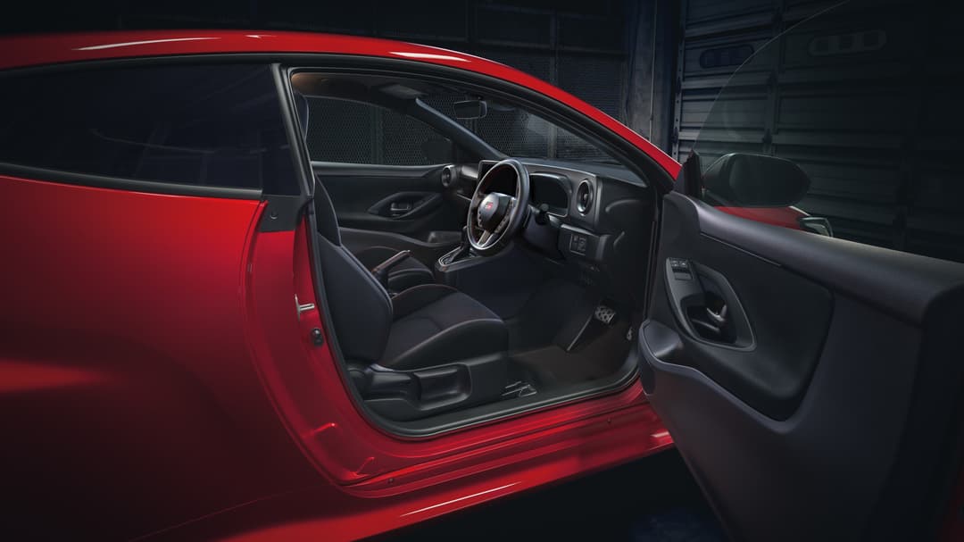 Intérieur de la Toyota GR Yaris avec volant GR, sièges noirs et tableau de bord moderne, portière ouverte révélant la carrosserie rouge