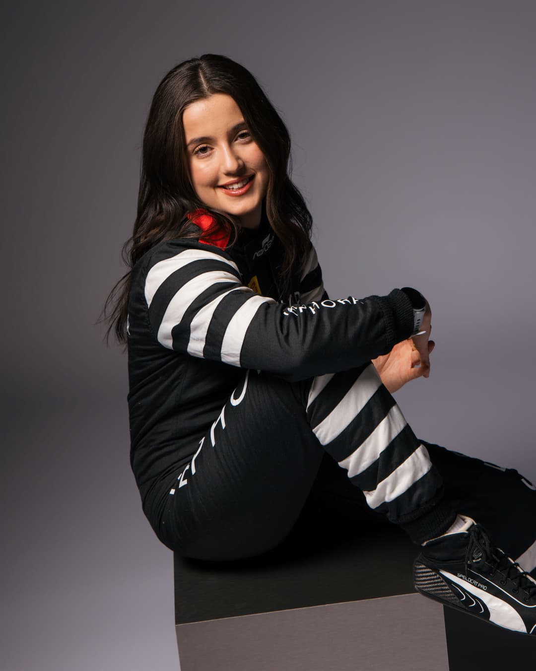 Natalia Granada en tenue de pilote F1 Academy Sephora noir et blanc à rayures, avec accents rouges, souriante en pose dynamique