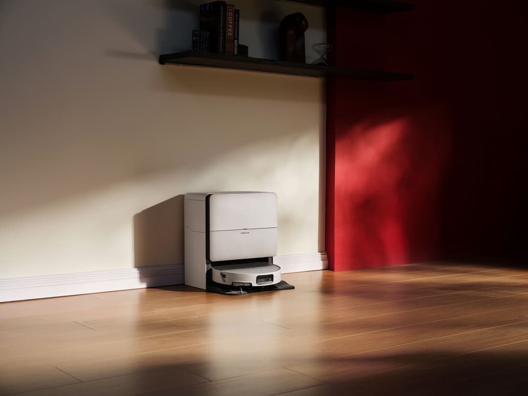 Robot aspirateur Roborock blanc et noir se déplaçant sur un parquet clair, station de nettoyage intégrée en arrière-plan