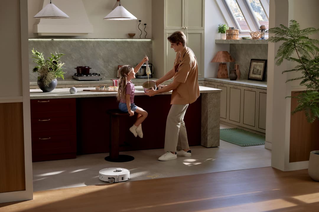 Robot aspirateur blanc Roborock qui fonctionne au sol d'une cuisine moderne tandis qu'une femme et une enfant discutent au comptoir