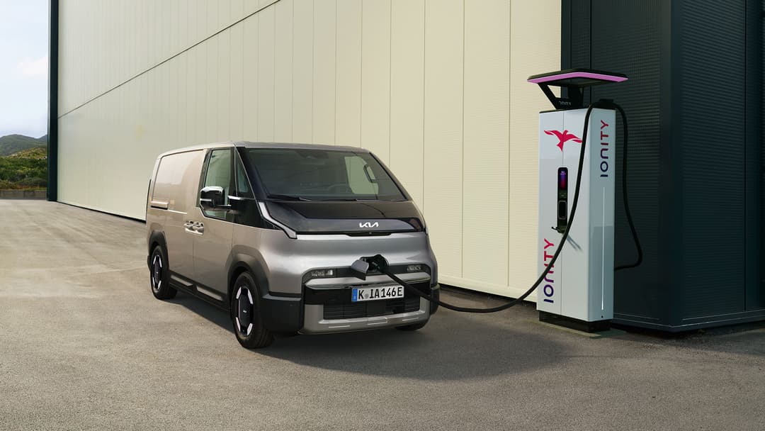 Kia PV5 Crew Van gris clair branché sur une borne de recharge Ionity, devant un bâtiment blanc