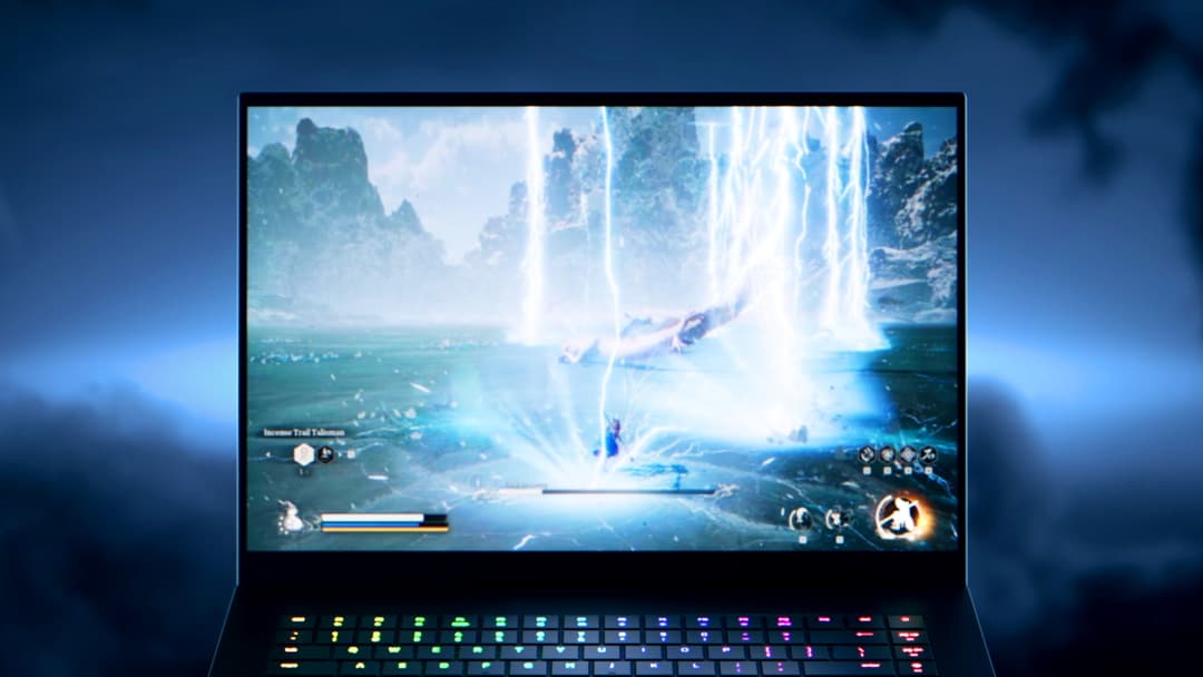 Razer Blade 16 ouvert affichant un jeu vidéo avec cascade lumineuse, clavier rétroéclairé multicolore en avant-plan