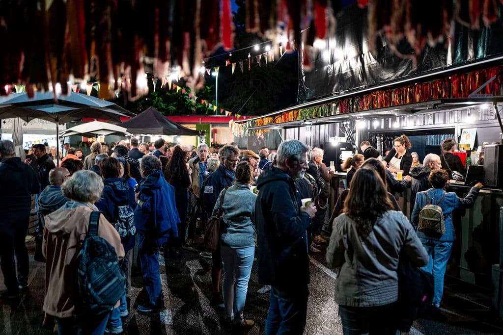 Foule visitant le festival Usinesonore la nuit, sous des guirlandes colorées, entre stands d'exposition et structures temporaires