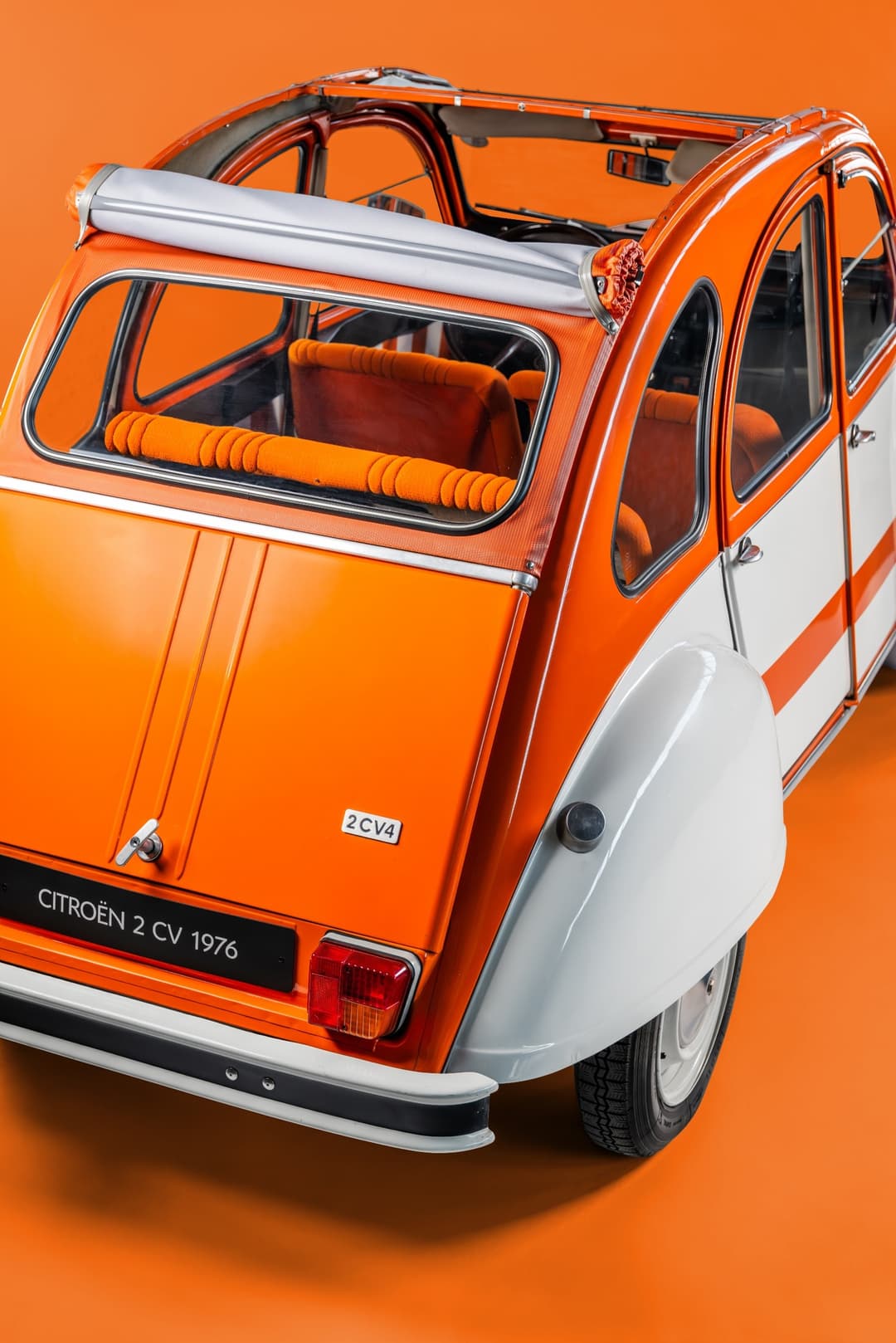 Citroën 2CV Spot 1976 orange et blanc, capote baissée, intérieur orange, vue de trois quarts arrière