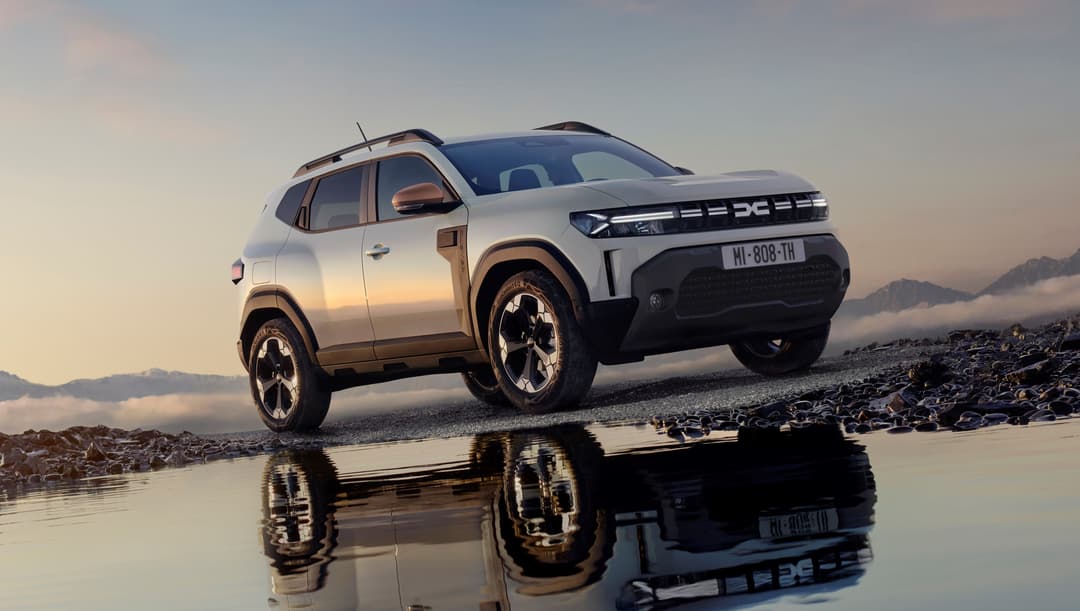 Dacia Bigster hybrid 150 4x4 blanc et noir garé sur un terrain rocheux en bord d'eau, montagnes en arrière-plan
