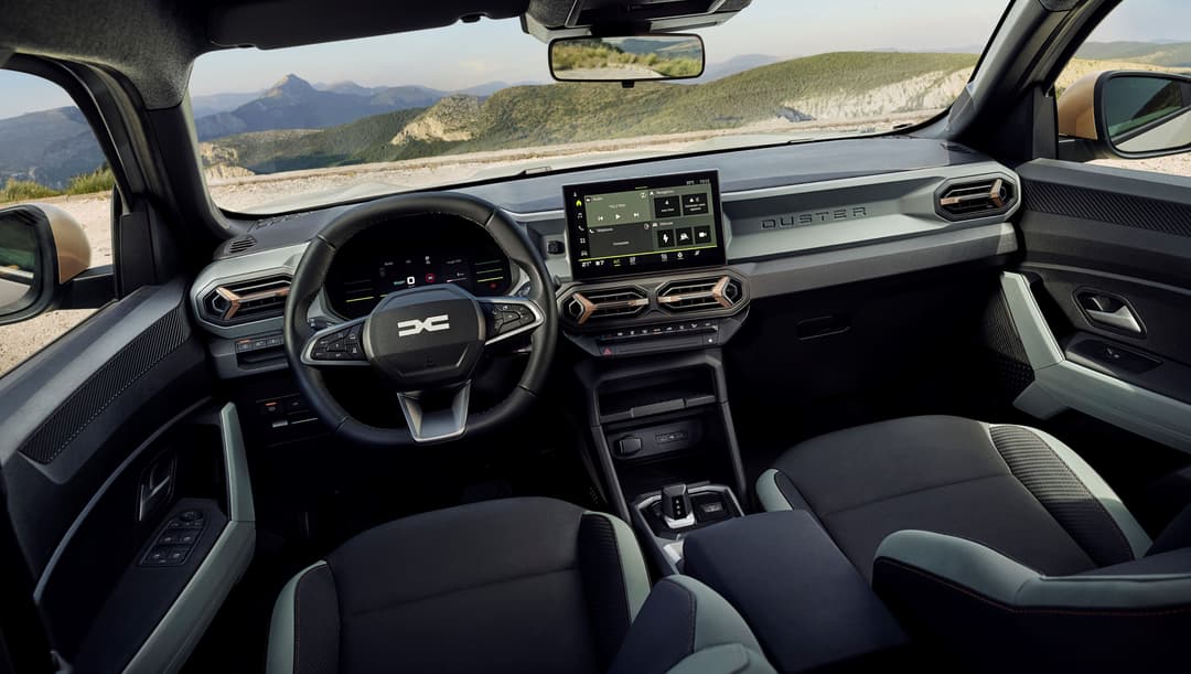 Intérieur du Dacia Duster hybrid 150 4x4 avec volant, écran tactile, sièges gris et noir, montagnes visibles par la fenêtre