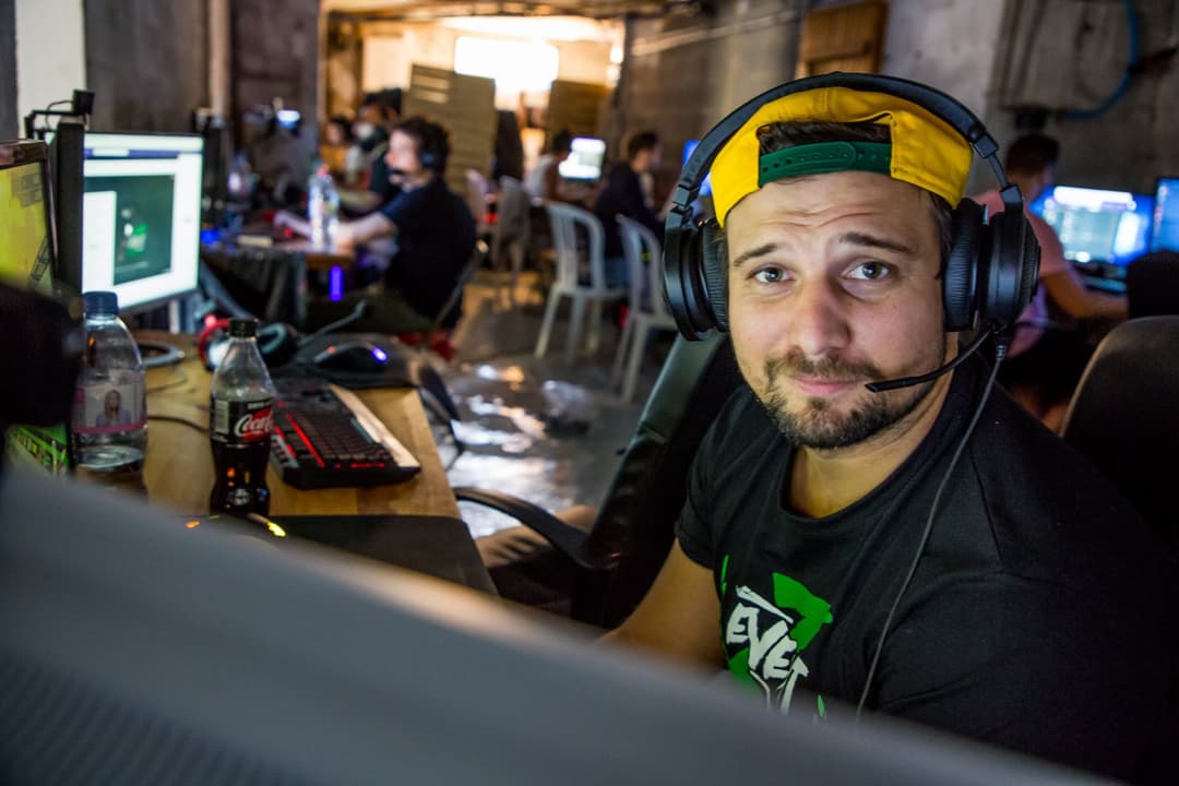 Streamer Gius avec casque et bandeau jaune, assis devant un écran d'ordinateur lors d'un événement gaming
