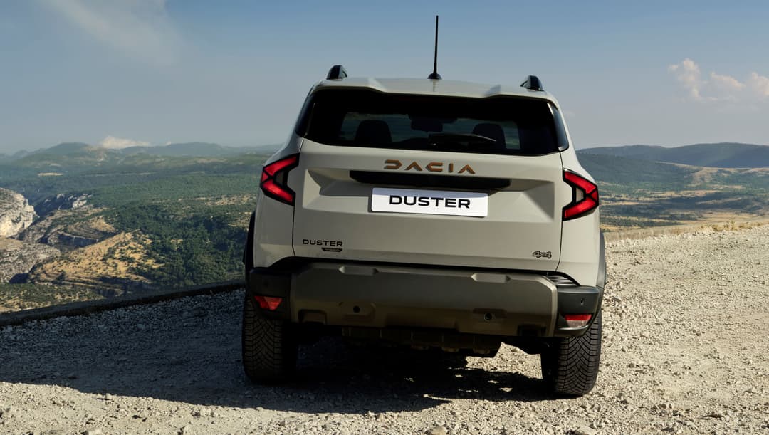 Dacia Duster blanc vue de l'arrière sur un chemin de montagne rocailleux, avec paysage montagneux en arrière-plan