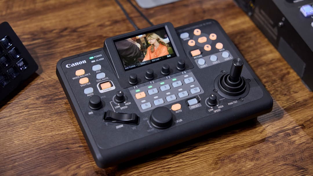 Contrôleur PTZ Canon RC-IP300 noir avec écran tactile affichant une vidéo, boutons de contrôle et joystick, posé sur un plan de travail en bois