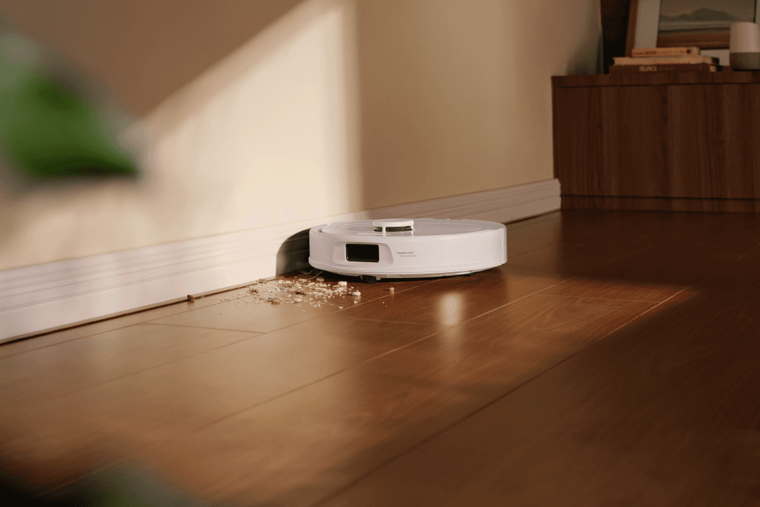 Roborock Qrevo S Pro blanc en action sur parquet, collectant des miettes près d'une plinthe