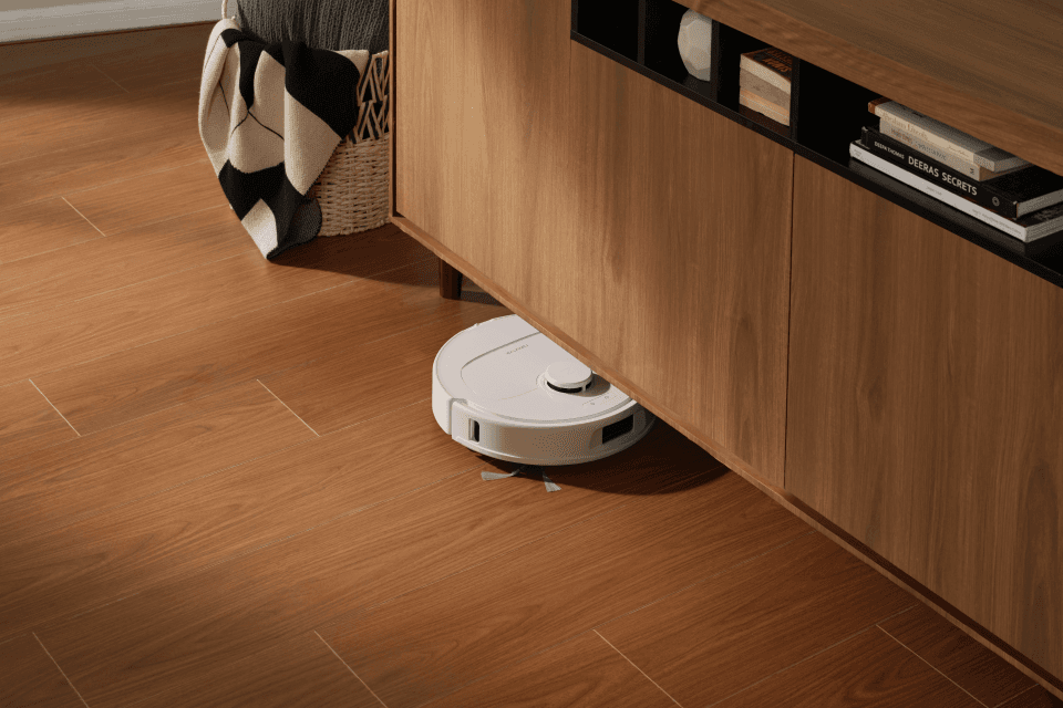 Robot aspirateur Roborock Qrevo S Pro blanc et noir circulant sous un meuble en bois sur un parquet clair