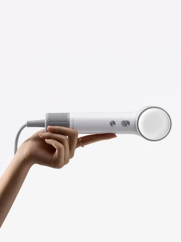 Main tenant un sèche-cheveux Dreame Pocket Neo gris avec embout diffuseur, sur fond blanc