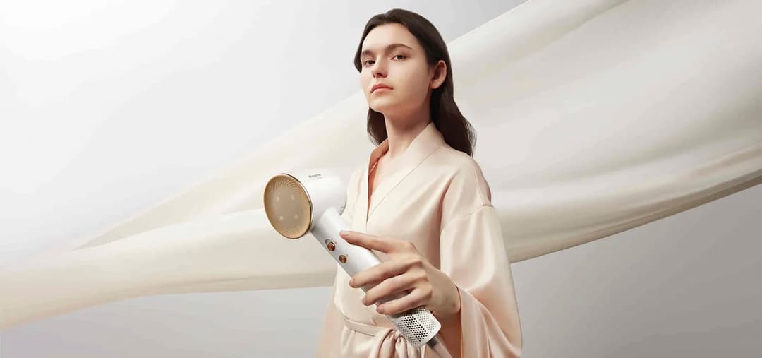 Femme tenant un sèche-cheveux blanc Dreame avec grille dorée, vêtue d'une robe beige clair